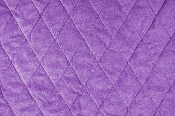 istock Quilted violet velours fabric background, wrinkled soft blanket surface 1648376007