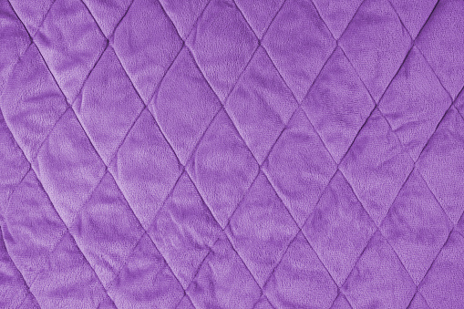 Quilted velours fabric background. Violet texture blanket or puffer jacket, stiched with diamond pattern, soft wrinkled surface, crupmed textile