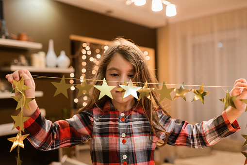 Cheerful girl standing on a chair and decorating the Christmas tree at home
