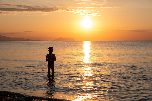 A child girl bathes in the sea in the morning and meets the dawn. Alicante Spain