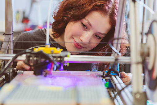 Close up of Gen Z  teenage girl watching three-dimensional printing in contemporary laboratory.
