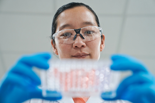 Low angle view of female scientist holding tray of medical samples in laboratory. Focus on background.