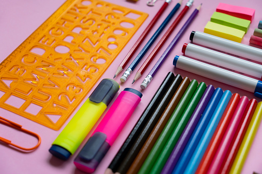 Office and school supplies arranged on pink background