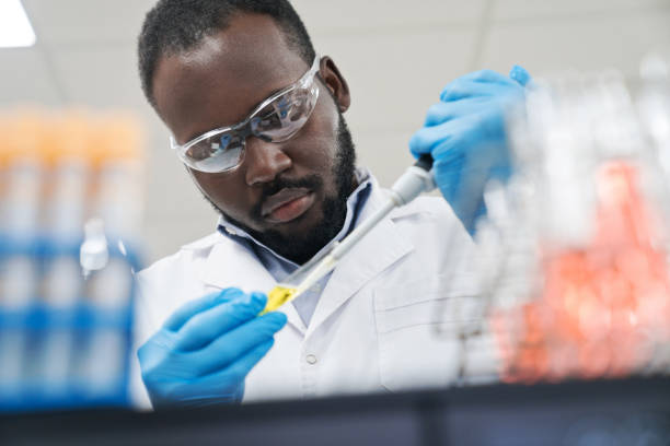 trabalhador médico do sexo masculino pipetando produto químico no tubo de ensaio enquanto trabalha no laboratório - genetic research men chemical protective glove - fotografias e filmes do acervo