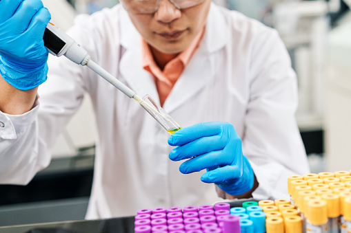 Midsection of female medical healthcare worker filling chemical in tray using pipette while working in laboratory