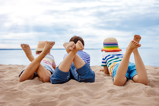 Three children lying on the sea beach in sunny day. Concept of the family vacation and tourism.