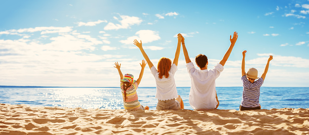 Parents with their child sitting in the sand on the seashore in sunny day. Concept of the family vacation and tourism.