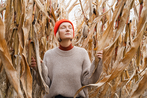 Portrait of relaxed and confident woman with eyes closed on background of dried corn field in autumn. Thoughtful person in front of agricultural field area. Concept of ecology, sustainable lifestyle.