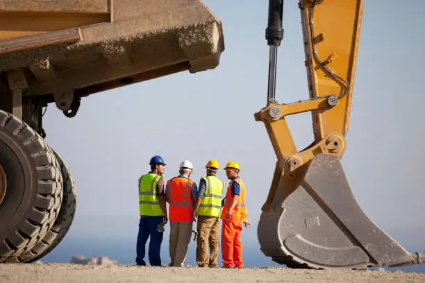 Photo of Workers talking by machinery in quarry