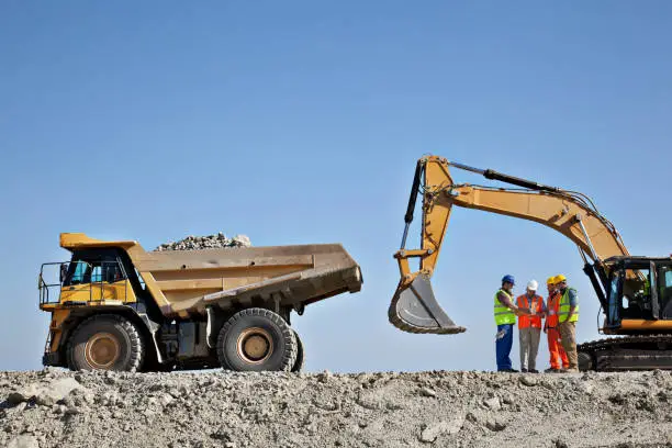 Photo of Workers talking by machinery in quarry