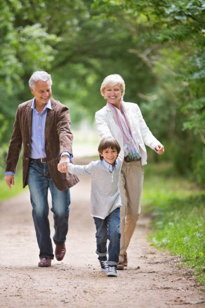 couple marchant avec petit-fils sur rural road - generation gap multi generation family vertical holding hands photos et images de collection