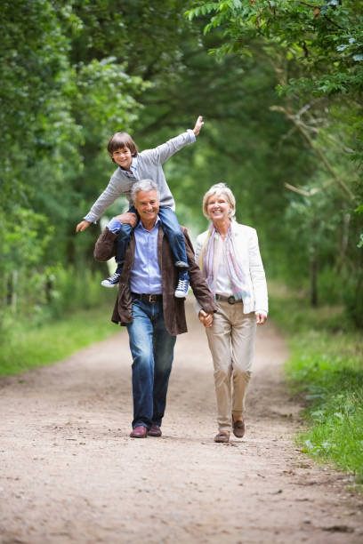couple marchant avec petit-fils sur rural road - generation gap multi generation family vertical holding hands photos et images de collection