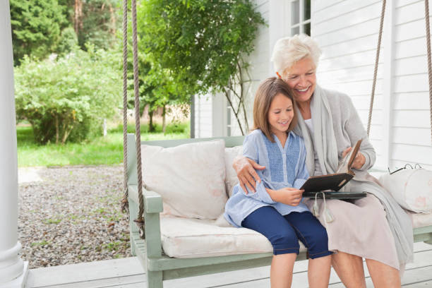 mujer y granddaughter lectura en columpio para la terraza - grandmother generation gap senior adult granddaughter fotografías e imágenes de stock