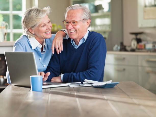 paar mit laptop in kitchen table - senior adult couple computer retirement stock-fotos und bilder