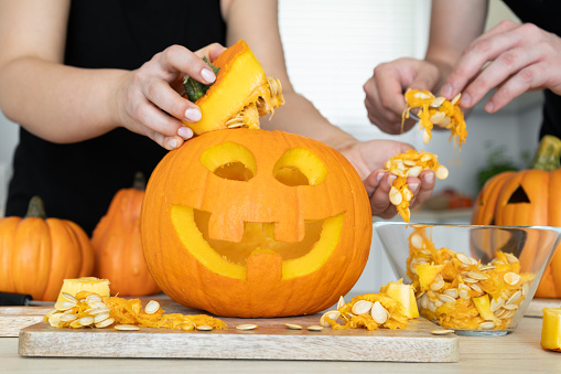 Couple gutting Halloween pumpkin, hollowing Jack-o'-lantern, removing guts and seeds from inside.