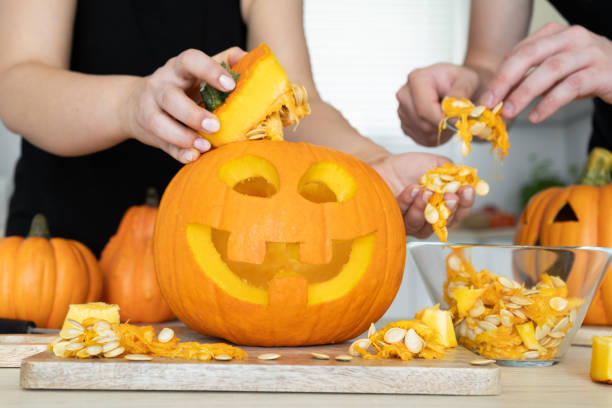 Couple gutting Halloween pumpkin, hollowing Jack-o'-lantern, removing guts and seeds from inside. Man and woman hands gutting Halloween pumpkin. Couple of people hollowing Jack-o'-lantern, removing guts and seeds from a Halloween pumpkin by reaching inside through the cut-off top lid. carving stock pictures, royalty-free photos & images