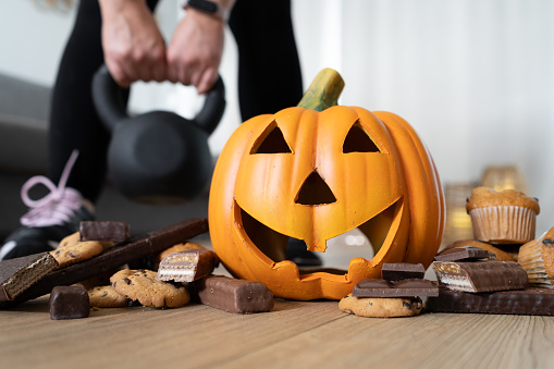 Woman exercising at home. Focus on Halloween pumpkin decoration and chocolate sweets. Healthy fitness autumn fall lifestyle, seasonal fit diet choice. Rejecting unhealthy food. Gym workout and sport training concept.