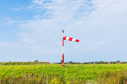 White and red wind flag (windsock)at the harbour of Spiekeroog, East Frisian Island, Germany. Air sleeve on a sunny day indicating direction of wind. Windy weather concept.