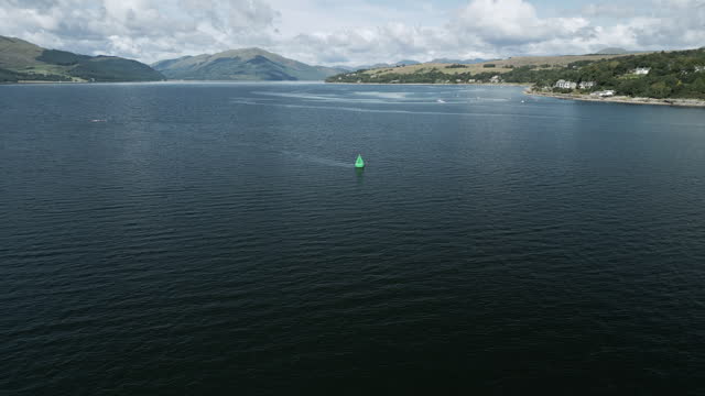 Drone footage over Scottish loch; passing over Stbd (green) navigation buoy. Scottish mountain (Cobbler) in the distance. Seagull flying by. 4K.