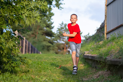 A happy boy runs and plays in the summer against the backdrop of green nature.