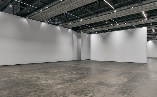 Side view of an empty white large gallery/showroom interior with white partitions empty walls for events or artwork exposure, and a ceiling industrial construction with reflectors (lights) on the dark gray cement tile floor. 3D rendered image.