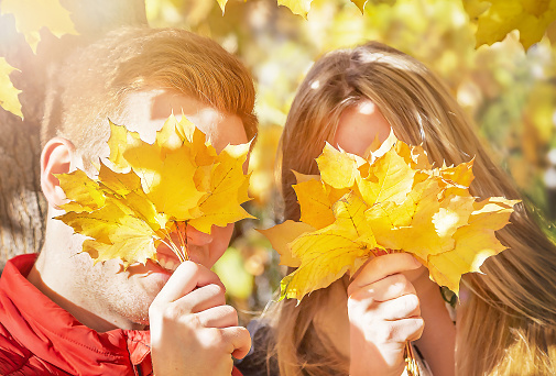 Happy autumn (fall) couple. Young woman (girlfriend) and man (boyfriend) having fun, enjoying in sunny autumnal day. Yellow leaves background. Outdoors.