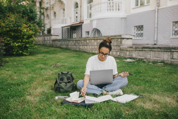 istock Young woman student studying using her books, laptop and notebook, sitting on grass. 1648670842