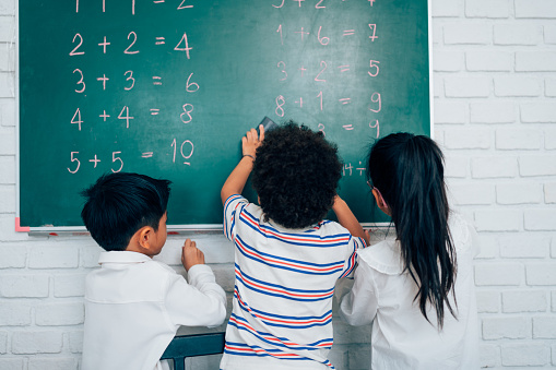 Group of little child standing at chalkboard and writing math formula on blackboard in classroom at school, education concept.