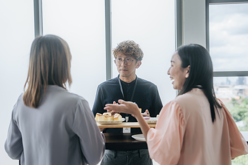 Asian man enjoying a snack break while two women chatting at table.