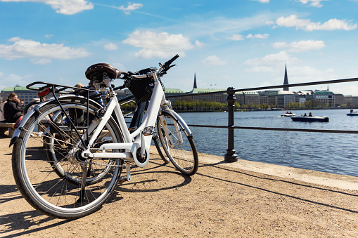 Scenic view two modern bicycles parked at embankment of Alster lake in Hamburg street old city center background summer day panorama view. Healthy travel lifestyle concept. Urban rental transport