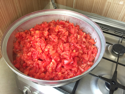 Chopped tomatoes cooking in a large saucepan for make tomato paste on stove burner