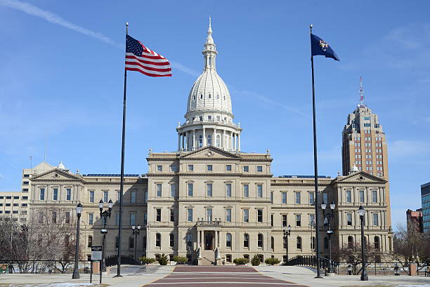 Michigan State Capitol in Lansing during Autumn, with green, golden, and red colored trees in the foreground.  The Michigan State capitol was built in the neoclassical / Italianite style.