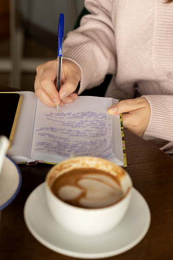 Women's hand writing in a blank notebook, home office lifestyle workspace