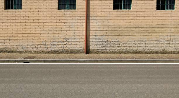 istock Old weathered yellow brick wall with red gutter in the middle. Sidewalk and street in front. 1648765859