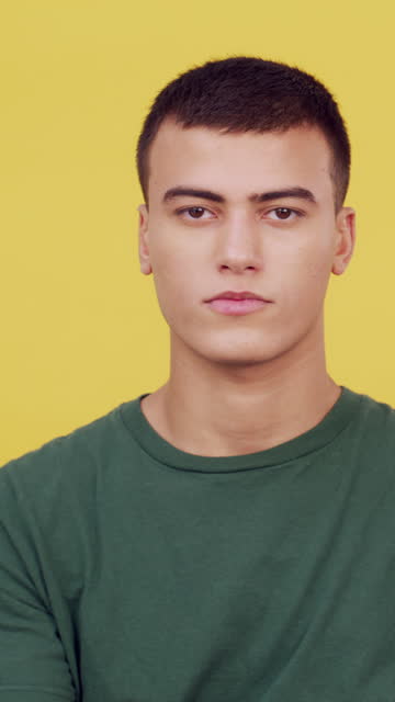 Face, serious fashion and man with arms crossed in studio isolated on a yellow background. Portrait, confidence and style of male model or person in casual clothes, cool tshirt and trendy in Brazil