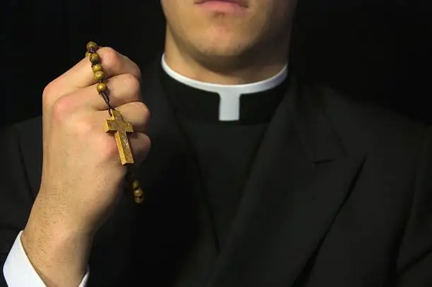 Young Priest praying with rosery in his hands