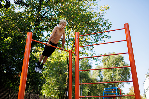A teenager on the crossbar performs acrobatic elements. Street workout on a horizontal bar in the school park.