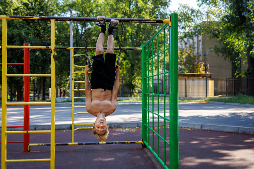 The boy hung upside down on the sports rings with his hands on them. Street workout on a horizontal bar in the school park.