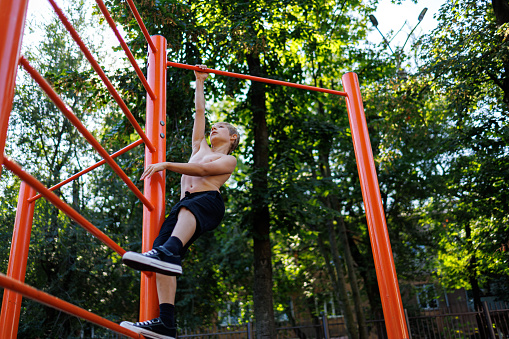 An athletic teenager tries to climb the crossbar. Street workout on a horizontal bar in the school park.