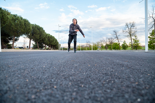 From below young cool male in sportswear riding on roller skates very fast on road in park