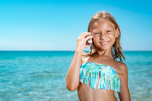 Cute little girl enjoying on the beach. She is poosing and looking at camera with smile on her face.