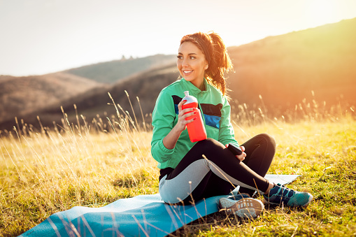 Young fitness woman resting and refreshing with water, after hard training on the meadow.