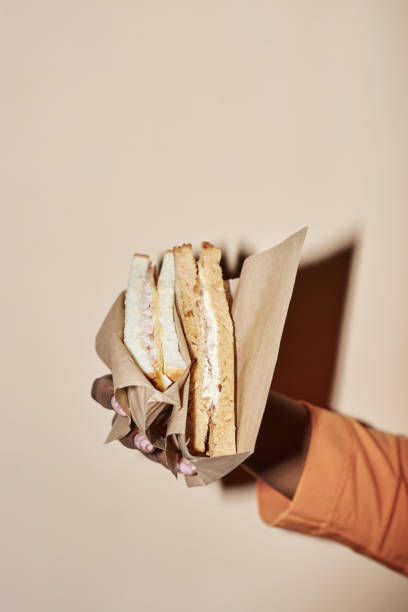 frau, die sandwich in papierverpackung hält - unhealthy eating flash stock-fotos und bilder