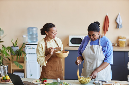 Waist up portrait of two African American women cooking together in cozy kitchen and having fun, copy space