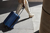 Cropped shot of young businessman in white pants pulling suitcase
