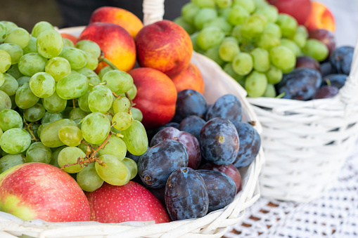 Different fresh fruits in white basket, grapes, apples, peaches and plums