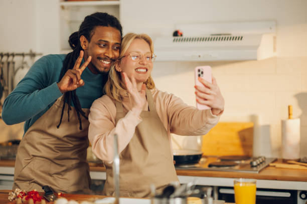 istock A cheerful interracial couple is having a video call with friends and greeting them while cooking food at home. 1648948053