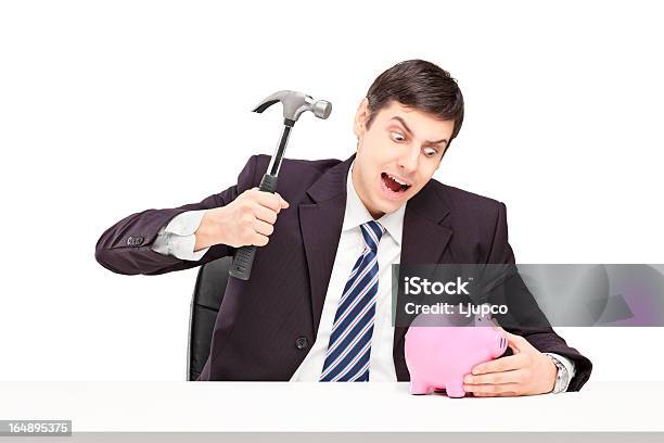 Irritated Man Trying To Break A Piggy Bank Stock Photo - Download Image Now - Breaking, Businessman, Coin Bank