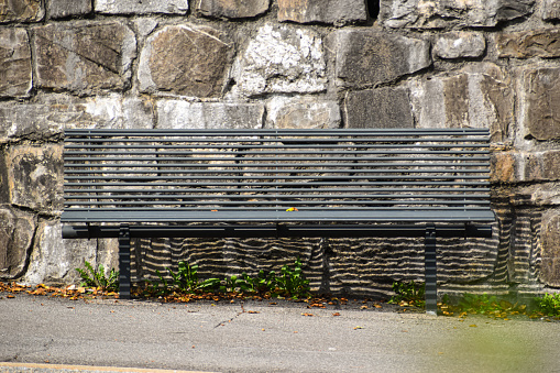 A grey painted metal bench in front of a stone wall at a public park