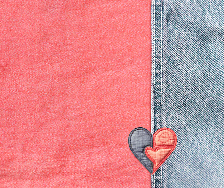 Pink and light blue denim background with a seam and felt heart. Coral and blue colors denim jeans fabric texture with heart-shaped textile patch. Valentine's day denim backdrop. Copy space for text